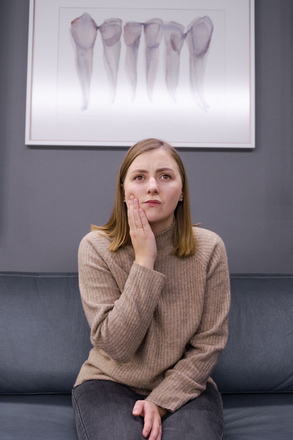 A woman on a sofa holding her hand against her cheek to ease tooth pain